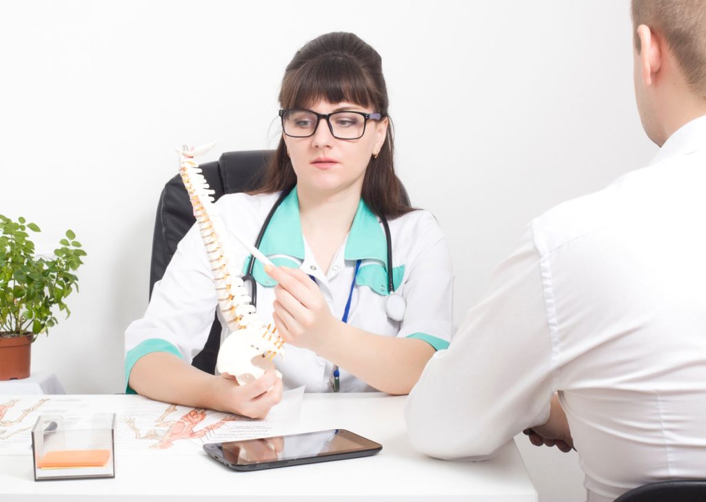 Doctor shows patient a diagram of the spine while explaining the difference between artificial disc replacement vs fusion