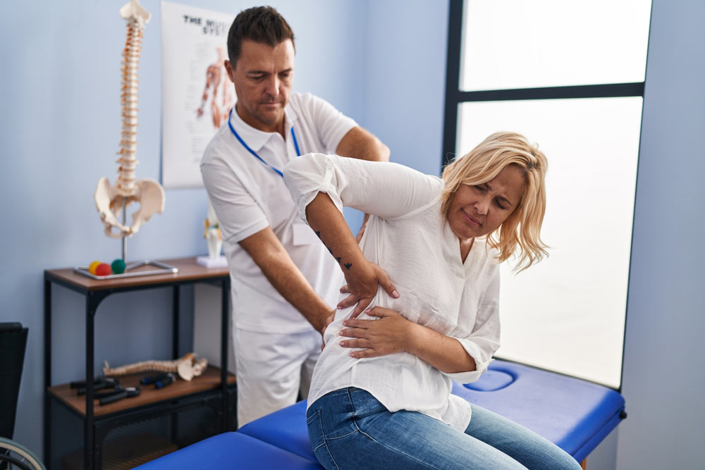 Middle aged woman holds her back showing a doctor where she is feeling pain