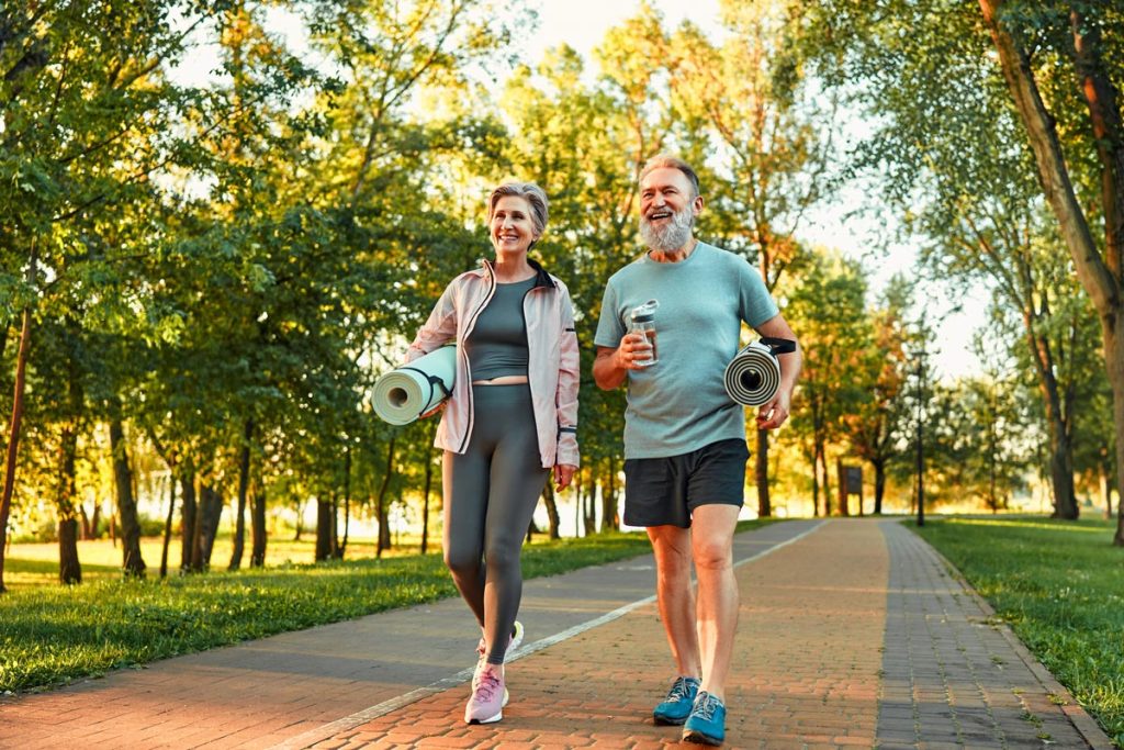 Cheerful older couple walking in the park holding yoga mats