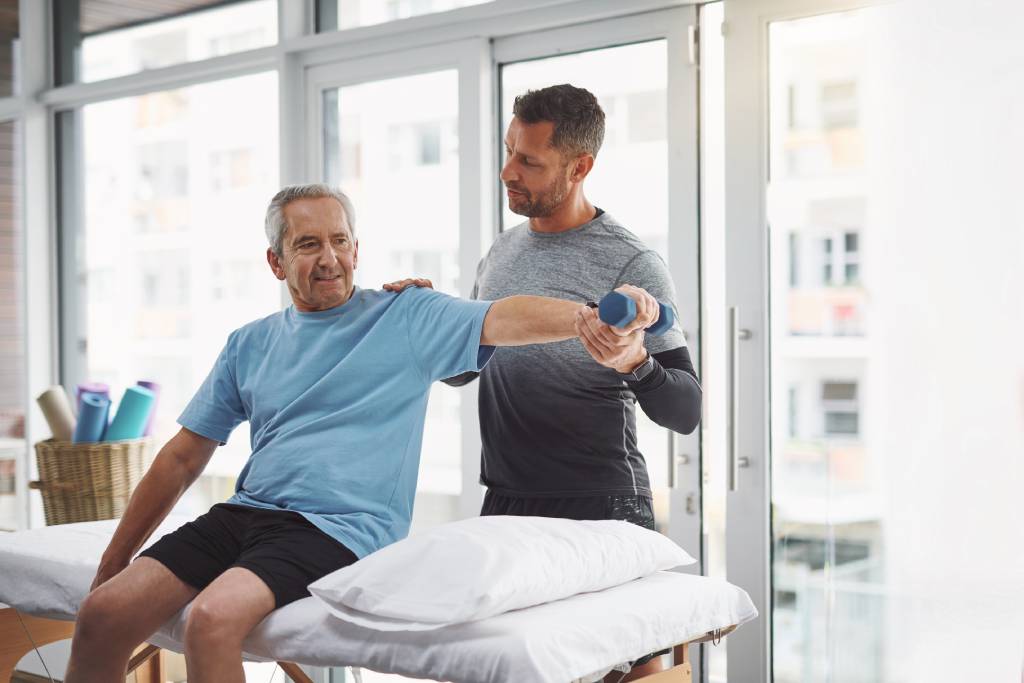 Physical therapist assists elderly man experiencing lower back pain